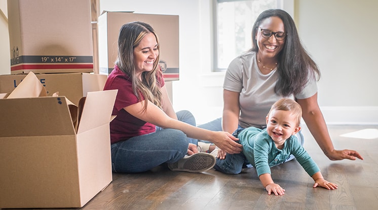 dos mujeres viendo gatear al bebé en el suelo entre cajas en movimiento