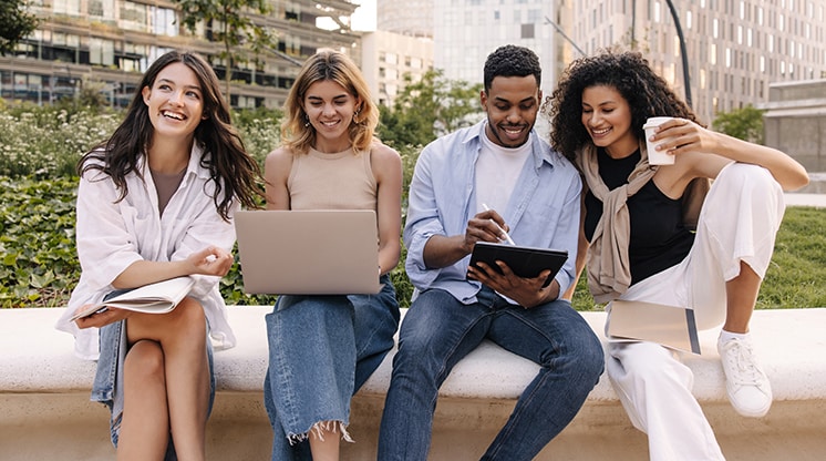 Cuatro amigos afuera con computadora portátil, iPad y café.